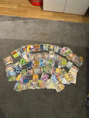 Stor samling Pokémonkort - Säljer en stor samling Pokémonkort med blandade typer, färger och motiv. Korten är av papper och har klassiska Pokémonillustrationer, energikort och tränarkort. Perfekt för dig som vill bygga din egen lek eller samla på olika generationer av Pokémonkort.