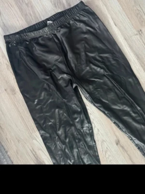 Svarta leggings i skinnimation l/xl  - Säljer ett par svarta leggings i glansigt skinimmation med resår i midjan. De har en tight passform och är perfekta för dig som vill ha en edgy look. Materialet är mjukt och stretchigt för extra komfort.