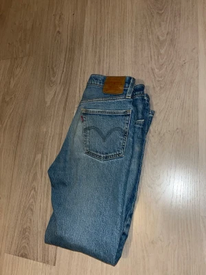 Levi's blå raka jeans - Klassiska blå Levi's jeans med rak passform och fem fickor. Jeansen har en vintage tvätt och den ikoniska läderlappen bak i midjan. Tillverkade i slitstark denim med den typiska röda Levi's-taggen på bakfickan. Perfekta för en avslappnad och tidlös stil.