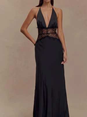 Svart långklänning med spetsdetaljer - Elegant svart långklänning med djup v-ringning och tunna halterneckband. Klänningen har öppen rygg och vacker spets i midjan som ger en unik look. Tillverkad i ett glansigt material som faller snyggt längs kroppen. Storlek S. Aldrig använd då den inte passade mig:(