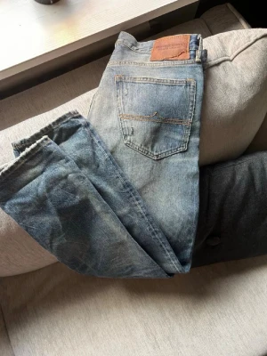Ljusblå vintage jeans från Ralph Lauren  - Säljer ett par ljusblå jeans från Ralph lauren med slitningar och tvättade detaljer. Jeansen har klassisk femficksmodell, normal midja och raka ben. Tillverkade i bomull med en skön och avslappnad passform. Perfekta för en casual look.