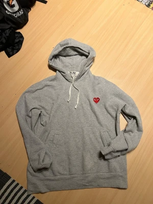 Grå hoodie från Comme des Garçons Play - Tjaaa säljer en fet hoodie ifrån comme des garçons, den är grå och väldigt snygg och bra material. Inge skada eller något på den🧼🧼det står storlek Xl men passar M-L passar om man är 180-190😊 hör av er vid frågor 🤝