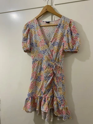 Blommig omlottklänning - Jättefin blommig sommarklänning. Inte alls mycket använd då den inte passar längre. Har satt dit en knapp som är i stort sett osynlig vid urringningen