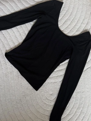 Svart ribbad långärmad topp - En svart, ribbad långärmad topp med rundad, djup urringning. Toppen har en slim passform och är tillverkad i ett mjukt, stretchigt material.