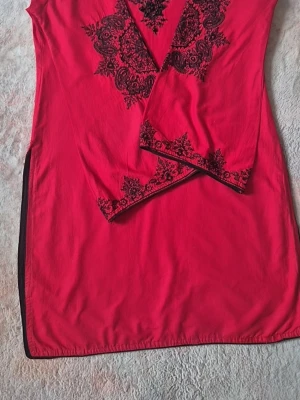 Red tunic - Red tunic with black embroidery and pearl details around the neckline and on the sleeves. The tunic has long sleeves and a straight fit. Black details along the side seams and bottom edge. Arm length: 49 cm  Shirt Length: 83 cm  Shipping same day if you order during opening hours of post office