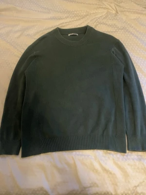 Mörkgrön stickad tröja från Zara - En stilren mörkgrön stickad tröja från Zara med rund halsringning och ribbade muddar vid ärmslut och nederkant. Tröjan har en enkel och clean design som passar perfekt till lager på lager och är gjord i mjukt material.