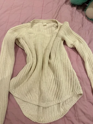 Vit stickad tröja med rund hals - Säljer en krämvit stickad tröja med rund hals och lång ärm. Tröjan har ett luftigt, ribbstickat mönster och längre bakstycke för en avslappnad look. Perfekt att slänga på sig över ett linne eller t-shirt.