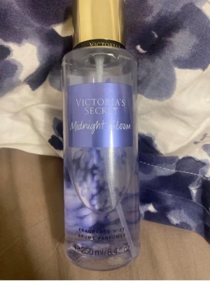 Victoria's Secret Midnight Bloom mist - Victoria's Secret Midnight Bloom är en doftmist i en genomskinlig plastflaska med lila och guld detaljer. Flaskan rymmer 250 ml och har en elegant, feminin design med blommigt motiv. Perfekt för dig som vill ha en fräsch och blommig doft.