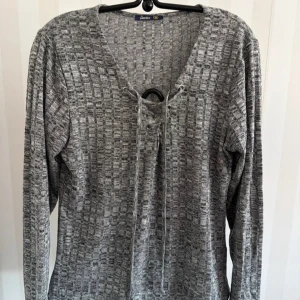 Grå långärmad tröja med snörning - Grå långärmad tröja från Lindex med strukturerat mönster och snörning i v-ringningen. Tröjan har en avslappnad passform och är tillverkad i mjukt material som passar perfekt till jeans eller kjol.