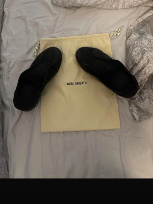 Svarta sneakers från Axel Arigato - Stilrena svarta sneakers från Axel Arigato i mocka med minimalistisk design. Skorna har låg profil och svart sula, perfekta för dig som gillar en clean och modern look. Kommer med original dustbag. tyvärr ingen box