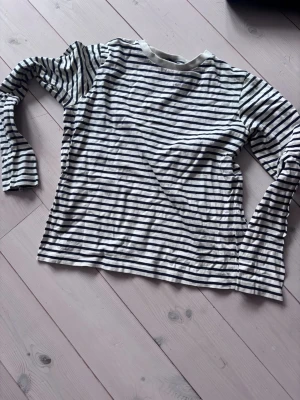 Randig långärmad topp från Ivy - Säljer en vit långärmad topp från Ivy med svarta horisontella ränder. Toppen har en klassisk rund halsringning och är gjord i mjuk bomull. Perfekt att styla med jeans eller kjol för en enkel och snygg look.