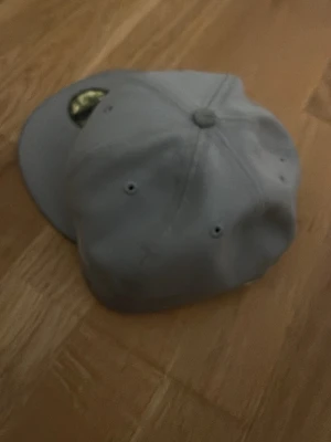 Grå LA-keps från New Era - Säljer en stilren grå keps från New Era, modell 59FIFTY med LA-logga broderad framtill i vitt. Kepsen har rak skärm och klassisk sexpanelsdesign med ventilationshål. Perfekt för dig som gillar streetwear och sportig stil.