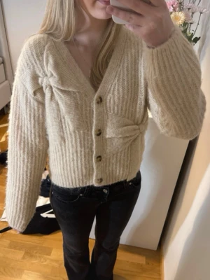 Beige ribbad kofta med knappar - Mysig beige kofta med ribbad struktur och dekorativa knytningar framtill. Koftan har v-ringning, långa ärmar och träknappar. Perfekt för lager på lager och en avslappnad stil. Är i storlek 164 men passar xs/s! Lämna gärna prisförslag!