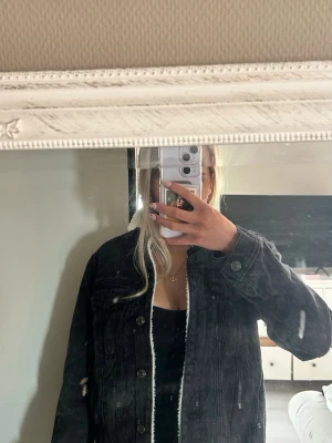 Svart teddyjacka med vit fuskpäls - Säljer en svart teddyjacka med vit, mjuk fuskpäls på insidan. Jackan har knappar framtill, två bröstfickor och en rak passform. Perfekt för dig som vill ha en varm och stilren jacka med en cool vibe. Finns ej att köpa längre 