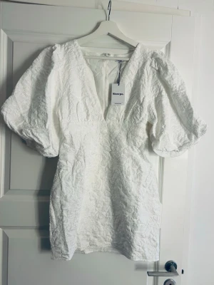 Vit kort klänning från Showpo - Supersnygg vit kort och eftertraktad klänning från Showpo med puffiga ärmar och v-ringning. Klänningen har ett strukturerat tyg med diskret mönster och dragkedja i ryggen. Perfekt för dig som vill sticka ut med en trendig och elegant look. Ge gärna prisförslag 🙌🏻💕