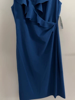 Ralph Lauren, klänning - Snygg klänning från Lauren Ralph Lauren med volangdetaljer längs ringningen. Klänningen är ärmlös och har en elegant, figurnära passform som ger en stilren siluett. Perfekt för dig som vill ha en klassisk look med en twist. Stl. 8.