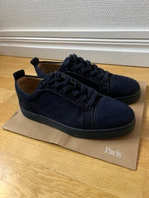 Mörkblå mockasneakers från Louboutin - Stilrena mörkblå sneakers i mocka från Christian Louboutin. Skorna har rund tå, matchande mörkblå snörning och diskret logga på insidan. Snygg och enkel design med svart sula och läderfoder för extra komfort.