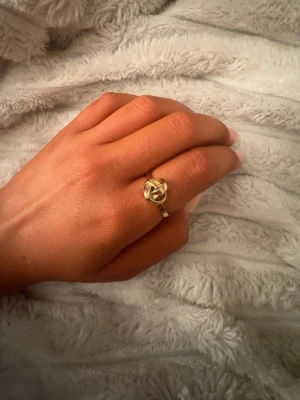 Guldfärgad ring med knutdesign - Snygg guldfärgad ring med unik knutdesign. Ringen har en elegant och modern look med en rundad form och glänsande finish. Perfekt accessoar för dig som gillar stilrena detaljer och vill sticka ut lite extra. Slutsåld!