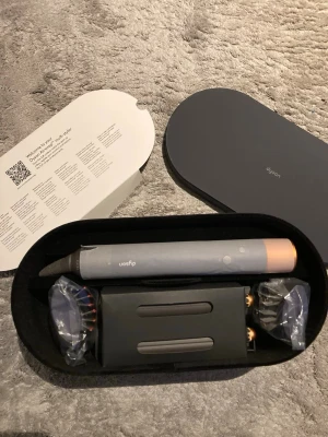 Dyson Airwrap hårstyler med tillbehör - Säljer en Dyson Airwrap hårstyler i snygg grå och kopparfärg med flera borst- och locktillbehör. Kommer i originalförpackning med praktisk förvaringsbox. Perfekt för att skapa olika frisyrer med både volym och lockar.