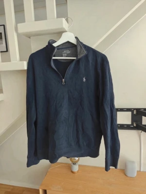 Ralph Lauren half zip - Mörkblå stickad tröja från Polo Ralph Lauren med halv dragkedja och ståkrage. Tröjan har lång ärm och den klassiska broderade loggan på bröstet. Perfekt för lager på lager och en stilren look.