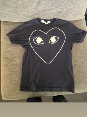 Mörkblå  Comme des Garçons Play t-shirt - Cool svart t-shirt från Comme des Garçons Play med det ikoniska hjärtmotivet med ögon på bröstet. T-shirten är i mjuk bomull och har en klassisk passform med korta ärmar. Perfekt för dig som gillar streetwear och vill sticka ut.