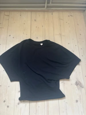 Svart t-shirt från Nelly - En svart basic t-shirt från Nelly i storlek XS. T-shirten har korta ärmar och en klassisk rund halsringning. Perfekt att matcha med jeans eller kjol för en enkel och stilren look.
