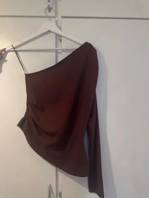 oneshoulder topp Gina Tricot - Snygg oneshoulder topp från Gina Tricot med en lång ärm och en smal axelrem. Toppen har en draperad passform och är tillverkad i mjukt polyestermaterial. Perfekt för dig som vill sticka ut med en trendig look.