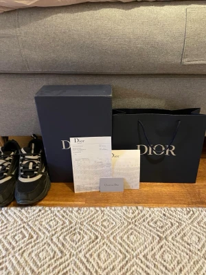 Svarta Dior B22 sneakers - Snygga svarta Dior B22 sneakers med chunky sula och meshdetaljer. Skorna har vita och grå inslag, samt reflekterande detaljer och tydlig Dior-logga på sidan. Perfekta för dig som gillar exklusiva och trendiga sneakers med sportig känsla.