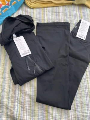 Svarta leggings från Lululemon - Snygga svarta leggings från Lululemon i stretchigt och mjukt material. Hög midja och figurnära passform, perfekta för träning eller chill. Diskret logga på benet och bekväm resår i midjan. Materialet är snabbtorkande och andas.