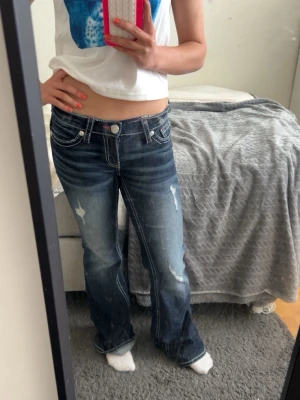 Mörkblå bootcut jeans med slitningar - Snygga mörkblå bootcut jeans med slitna detaljer och kontrastsömmar. Jeansen har låg midja och klassisk femficksdesign. Perfekta för en avslappnad och trendig look. De är klippta på sidan på båda kanterna men syns knappast enligt mig.