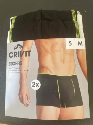Svarta boxerkalsonger från Crivit M - Tvåpack svarta boxerkalsonger från Crivit med gröna sömmar och resår. Tillverkade i COOLMAX-material som transporterar fukt och håller dig torr. Material: 48% polyester (COOLMAX), 47% bomull, 5% elastan (LYCRA). Perfekt passform och sportig design.