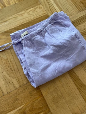 Ljuslila linnebyxor från Gina Tricot - Säljer ett par ljuslila linnebyxor från Gina Tricot. Byxorna har resår i midjan med dragsko och är tillverkade i ett luftigt linnematerial. Använt ett fåtal gånger.