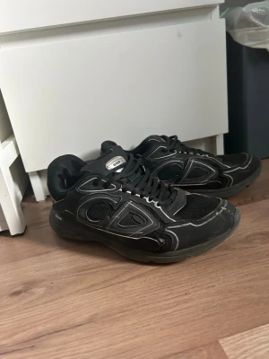 Svarta sneakers med vita detaljer - Svarta sneakers med vita kontrastsömmar och meshpaneler för extra ventilation. Skorna har en chunky sula och klassisk snörning. Märkeslogga på plösen och sidan. Perfekta för dig som gillar en sportig och retro stil. Mycket väl använda och har hål i sulan samt skador på sidorna storlek 42