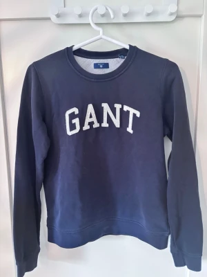 Mörkblå sweatshirt från GANT Storlek S - Mörkblå sweatshirt från GANT med vit broderad logga på bröstet. Klassisk rund halsringning och långa ärmar.