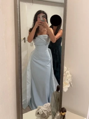 Ljusblå axelbandslös långklänning - Elegant ljusblå långklänning med axelbandslös design och draperad överdel. Klänningen har en figurnära passform upptill och ett utsvängt fall nertill, perfekt för speciella tillfällen.
