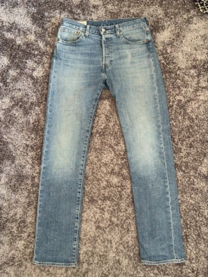 Ljusblå 501 jeans från levis - Säljer ett par klassiska 501:or från Levi's med raka ben. Jeansen har en snygg tvätt med lätt slitning framtill och bak, samt den ikoniska läderpatchen och röda Levi's-tag på bakfickan. Perfekta för en avslappnad stil. Storlek W29 L32