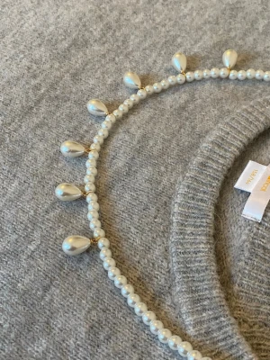 Pärlhalsband med droppformade hängen - Stilrent halsband med små runda pärlor och droppformade pärlhängen i vitt. Halsbandet har detaljer i guldton och ger en klassisk men trendig look. Perfekt för att lyfta vilken outfit som helst.
