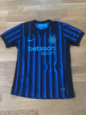 Inter Milan matchtröja Nike blå/svart - Snygg Inter Milan matchtröja från Nike i blått och svart med vertikala ränder. Tröjan har klubbmärke och Nike-logga på bröstet samt sponsortryck framtill. Tillverkad i lätt och ventilerande material, perfekt för fotbollsträning eller match.