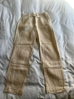 Beige linnebyxor med resårmidja - Snygga beige linnebyxor med rak passform och resår i midjan samt snöre. Byxorna har två sidofickor och är tillverkade i ett luftigt linnematerial som passar perfekt för en avslappnad stil. Lite tjockare än ett par vanliga. Köpt från A days merch. 