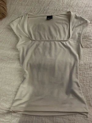 Vit topp med fyrkantig ringning Gina Tricot - Snygg vit topp från Gina Tricot med fyrkantig ringning och korta ärmar. Toppens material känns mjukt och stretchigt, perfekt att styla till jeans eller kjol. 