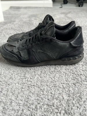 Valentino rockrunners  - Snygga helsvarta sneakers med coola nitar på hälen och detaljer i både läder och mocka. Skorna har lågt skaft och klassisk snörning. Perfekta för dig som gillar en stilren men edgy look.