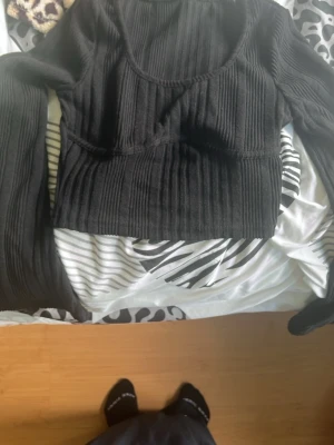 Svart ribbad croppad topp från SHEIN - Trendig svart croppad topp från SHEIN i ribbat material. Toppen har långa ärmar och en snygg, figurnära passform med rundad halsringning. Perfekt att styla med höga jeans eller kjol för en cool look.