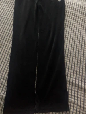 Svarta velourbyxor från Juicy Couture - Säljer ett par svarta mjukisbyxor i velour från Juicy Couture. Byxorna har raka ben och ikonisk Juicy-text i strass på baksidan. Perfekta för en chill och trendig look.