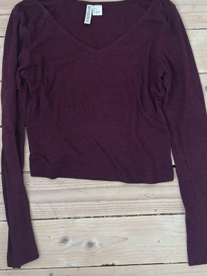 Vinröd v-ringad topp från HM Divided - Vinröd långärmad topp från Divided med v-ringning. Tillverkad i mjuk bomullsmix och har en slim passform som sitter snyggt på kroppen. Perfekt att matcha med jeans eller kjol för en enkel och stilren look.