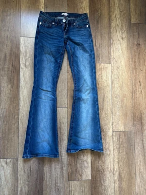 Blå bootcut jeans med röd söm - Säljer ett par blå bootcut jeans med snygga röda kontrastsömmar och broderad bakficka. Jeansen har klassisk femficksdesign.