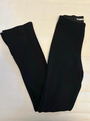 Svarta byxor med slits från Zara - Svarta byxor som liknar leggings med stretchigt material, smal passform och slits nertill från Zara i storlek S. 