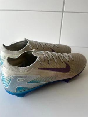 Nike Mercurial vapor 16 chromatic pack - Snygga Nike Mercurial fotbollsskor i silver med lila swoosh och blå detaljer på hälen. Skorna har låg profil, snörning och ovandel i lätt, ventilerande syntetmaterial för maxad speed på planen. Perfekta för dig som vill sticka ut och prestera.