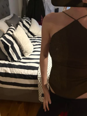 Brun glittrig body - Snygg brun glittrig topp med tunna axelband och öppen rygg. Toppen har en tight passform och är perfekt för dig som vill sticka ut. Materialet har en skimrande finish som fångar ljuset.