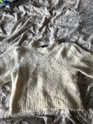 Krämvit fluffig stickad tröja - Mysig krämvit stickad tröja med fluffig textur och rak passform. Tröjan har rund halsringning och långa ärmar. Perfekt för lager på lager och ger en avslappnad men trendig look. Materialet ser ut att vara en mjuk ull- eller mohairblandning.