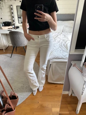 Vita bootcut jeans  - Säljer ett par vita jeans med utsvängd passform och medelhög midja. Jeansen har klassiska fem fickor och bälteshällor. Materialet är denim och de har en enkel, stilren look som passar till det mesta. Perfekta för dig som vill ha ett par ljusa jeans till sommaren.
